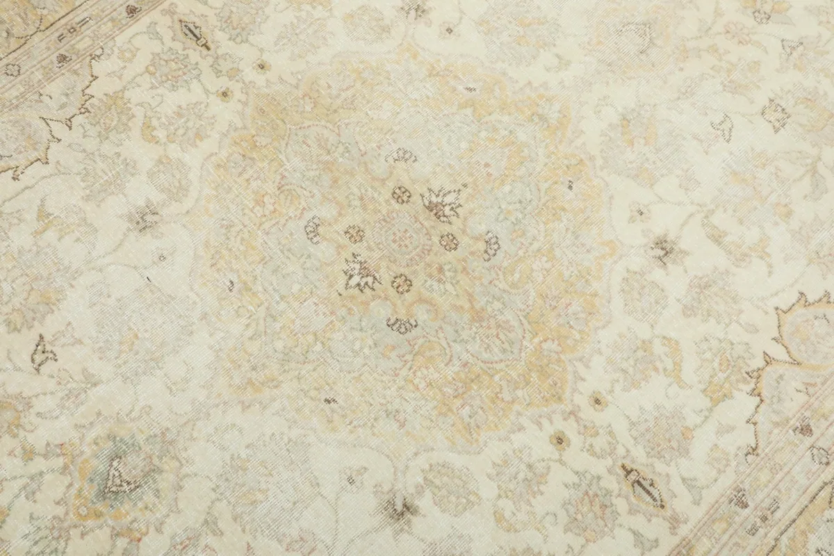 Detailed view of the central medallion design on the cream and gold vintage rug, showing faded colors.