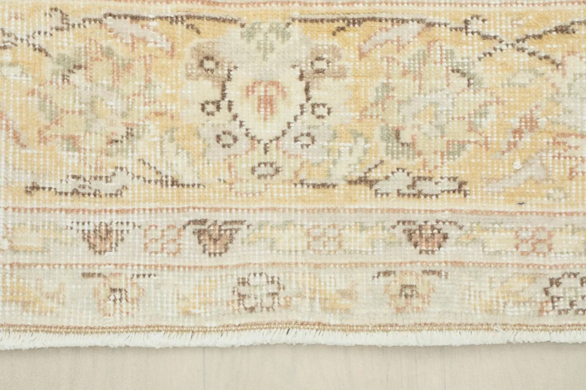 Detailed view of the outer border and edge of the cream and gold vintage rug, showing its hand-knotted construction.