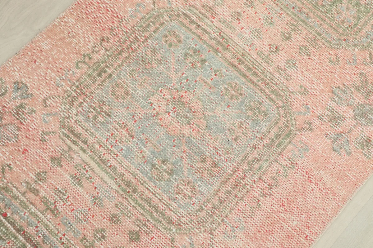 Detailed close-up of a faded green medallion motif on the rose field of the vintage runner.
