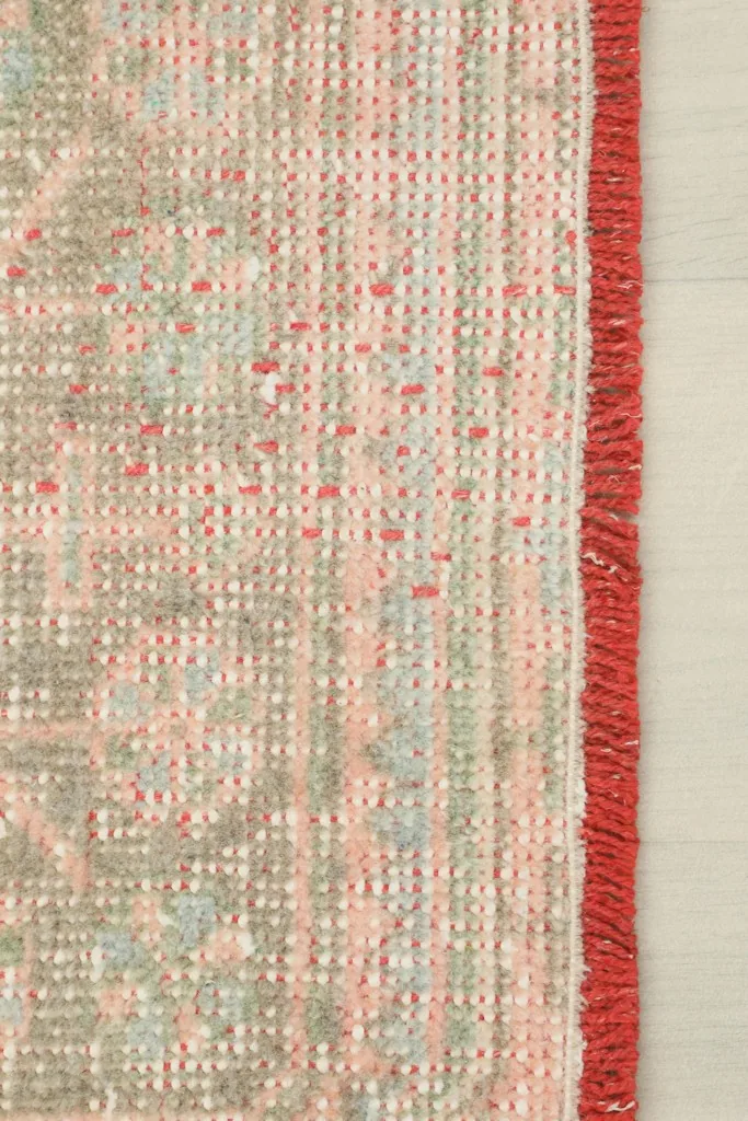Close-up of the rug's edge, showing the tightly woven side finish and the red binding.