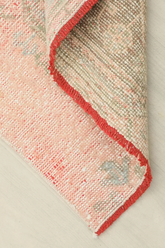 View of the rug's folded corner, revealing the cotton foundation and the reverse side of the knotting.