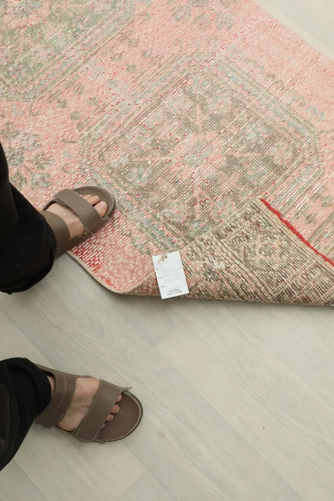 A person's feet next to the rug, showing its scale and a tag attached to the corner.