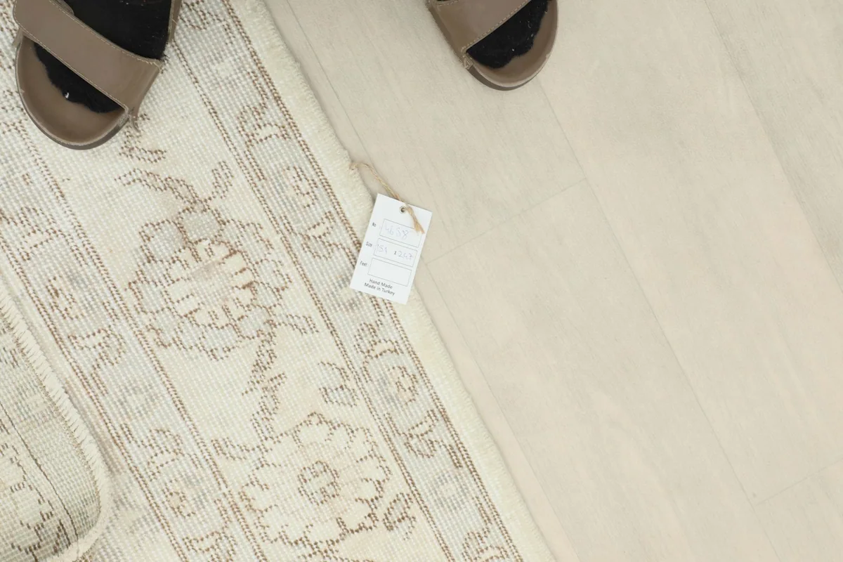 Overhead shot of the rug's edge with a size tag, next to a person's feet for scale.