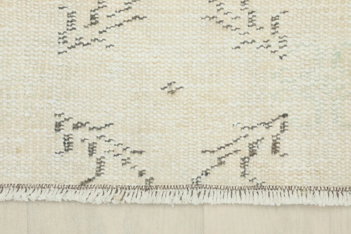 Detail showing the edge of the rug with its short, natural cream fringes and the charcoal border finish.