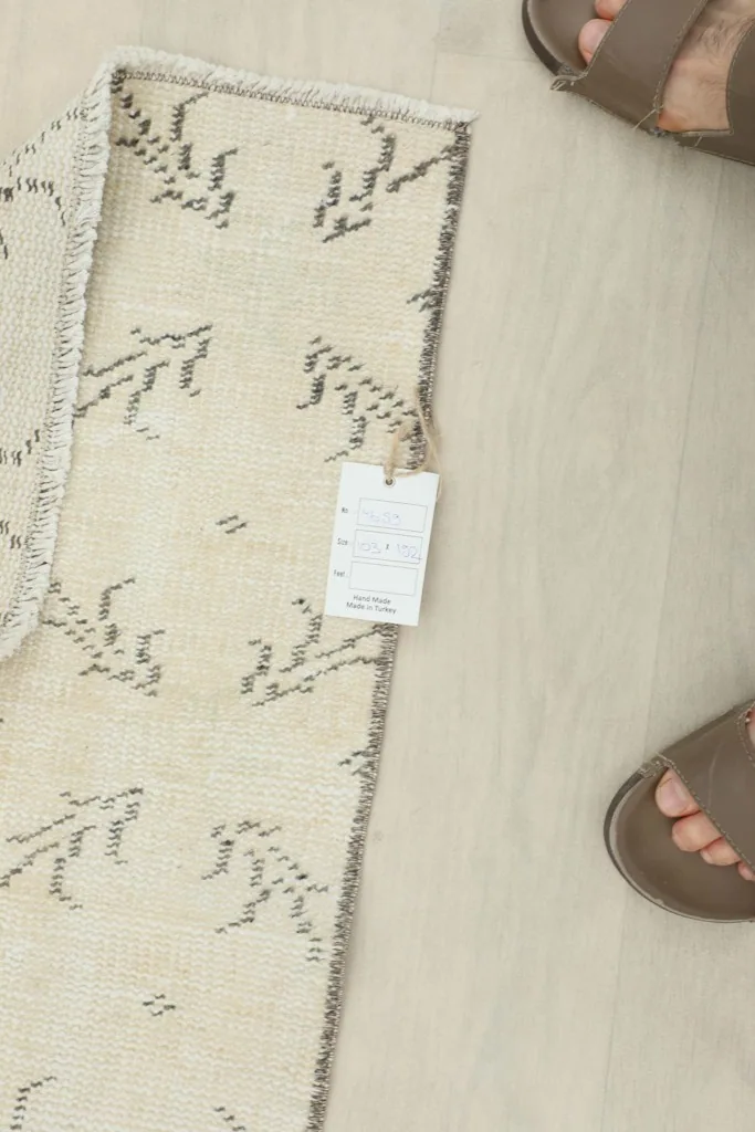 Top-down view of the rug with a tag attached and a pair of sandals nearby, indicating its small size.