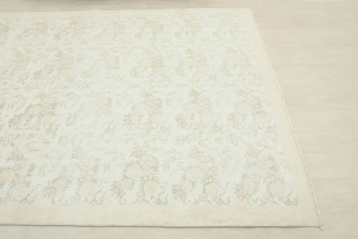 Close-up angle view of a corner of the ivory and tan vintage rug, highlighting the subtle floral pattern.