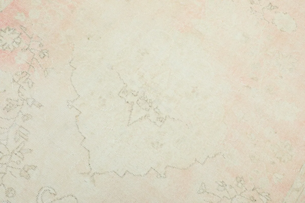 Detailed close-up of the rug's field, revealing the distressed ivory and rose colors and faint patterns.