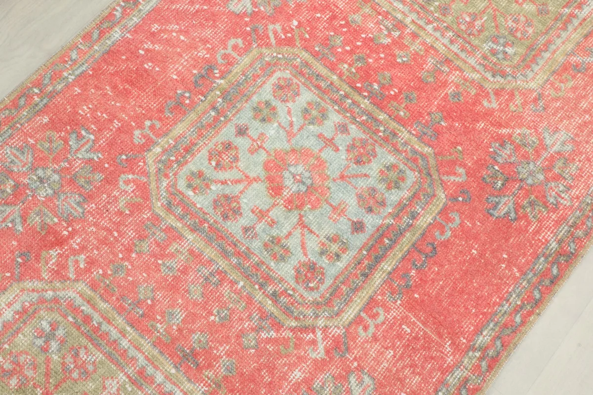 Detailed view of a central geometric motif in cream, rose, and olive on the rug's field.