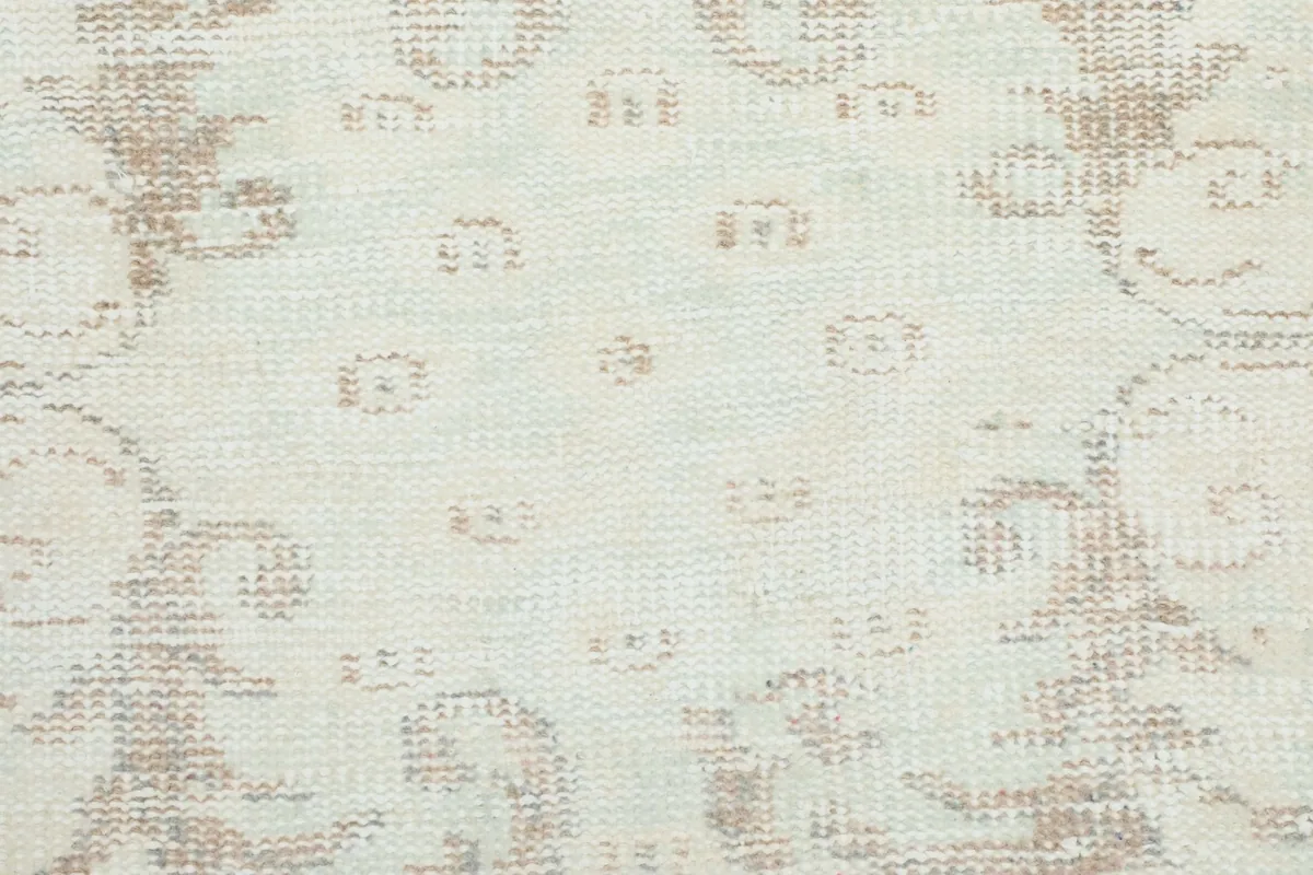 Extreme close-up of the low pile and intricate, faded patterns on the ivory beige rug surface.