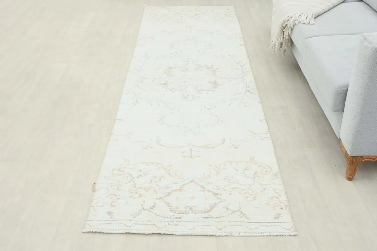 Full overhead view of the ivory beige runner rug in a room setting, next to a sofa.