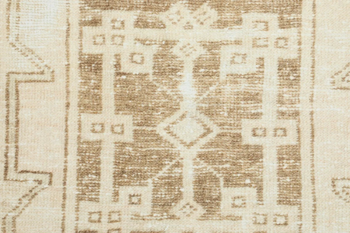 Close-up of the hand-knotted wool pile, showcasing the texture and faded tan geometric design.