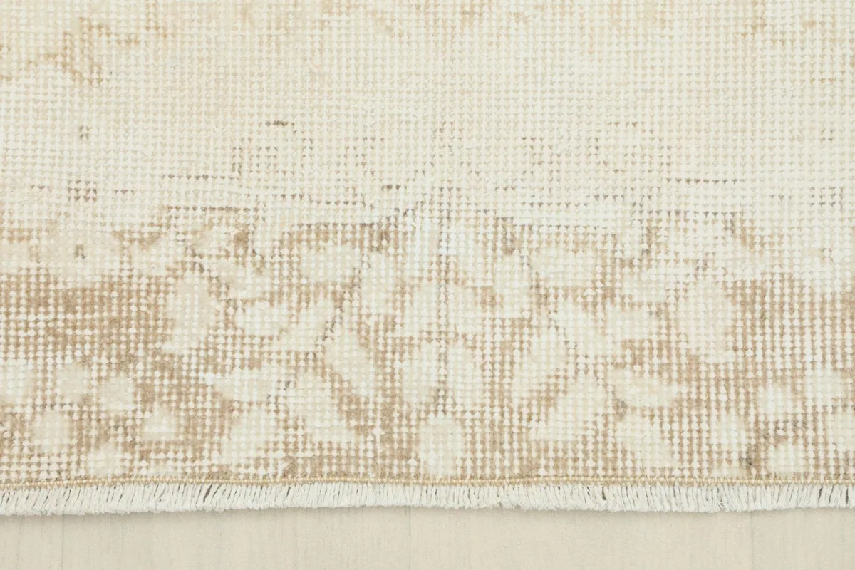 Detail of the rug's border and fringe, showing the worn texture and muted colors