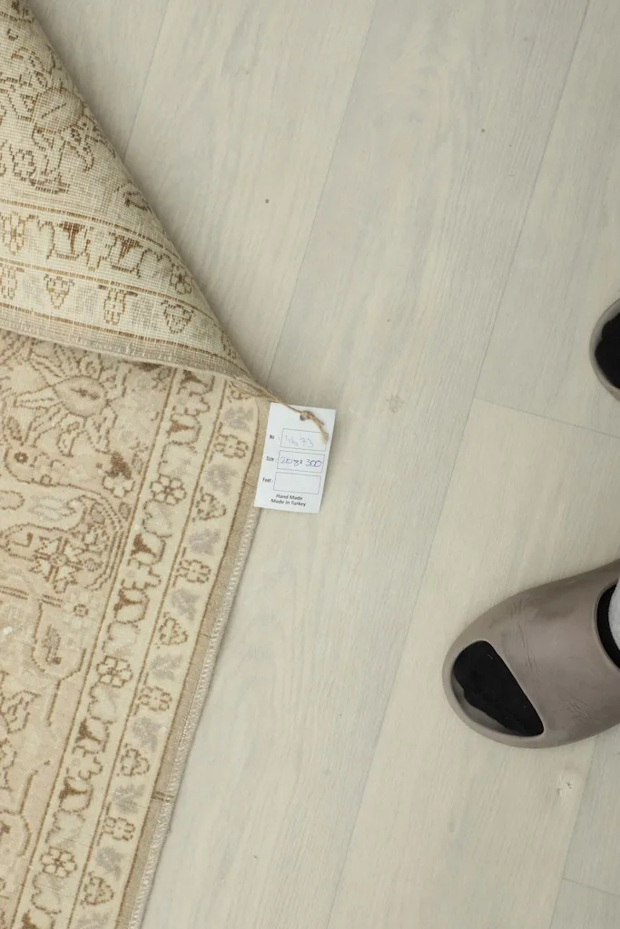 Top-down view of the rug's corner with a product tag and a pair of feet on the floor