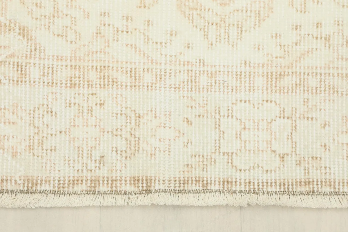 Close-up of the rug's edge, revealing the tan border design and the short, natural fringe.