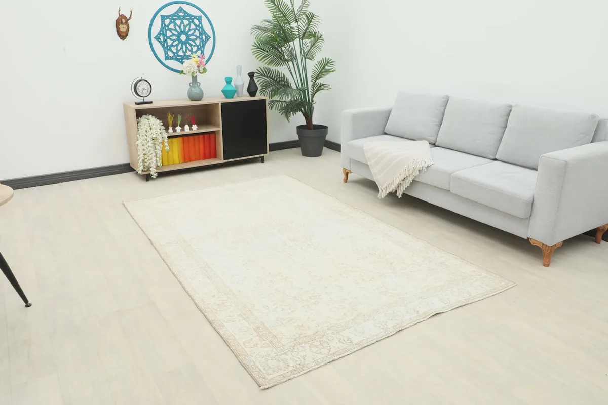 Vintage ivory rug displayed in a living room setting with a light gray sofa and wooden cabinet