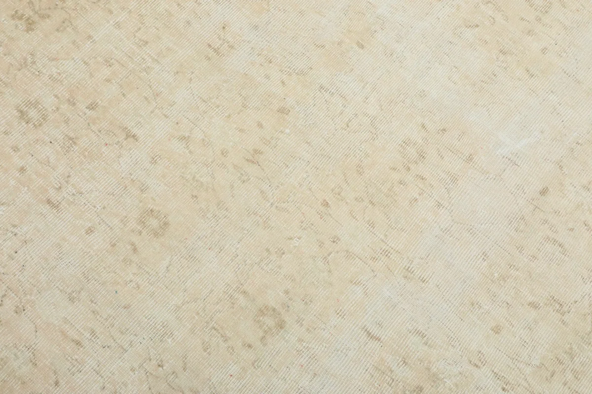 Detailed view of the rug's surface, revealing the hand-knotted wool pile and faded beige and ivory tones.