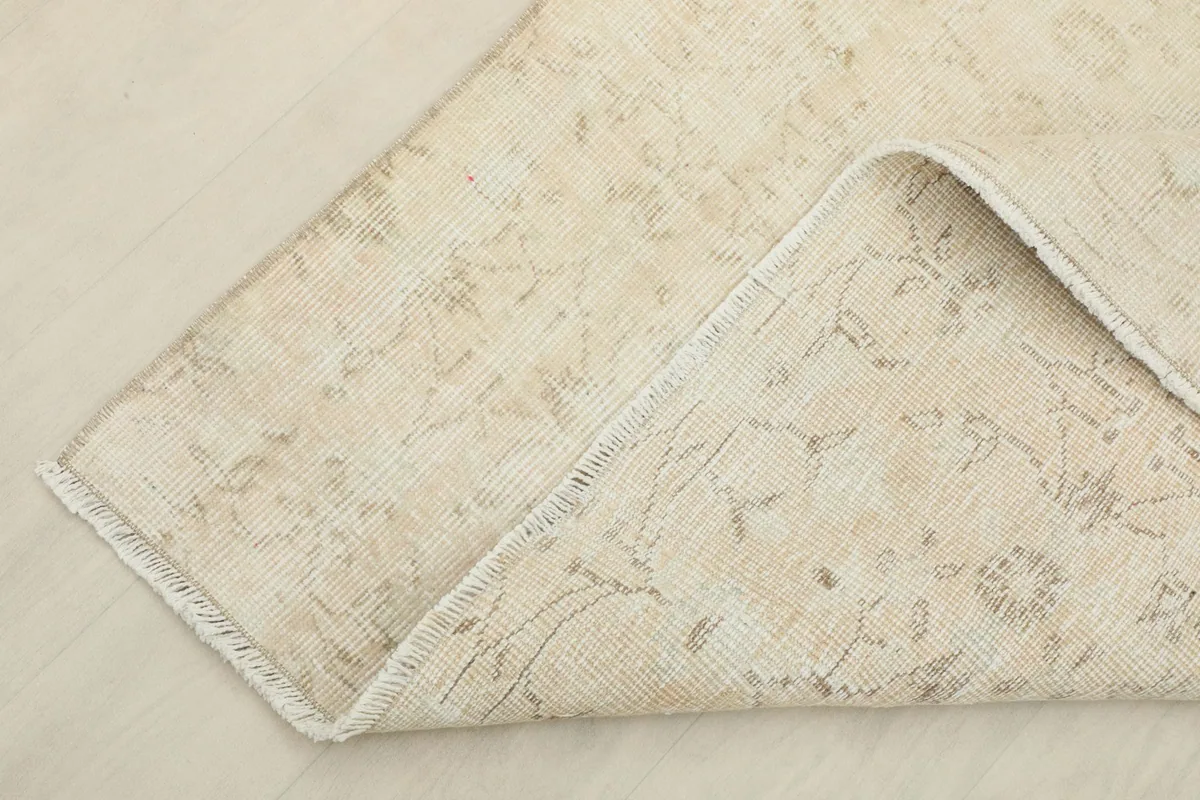 Corner of the rug folded back, revealing the reverse side with visible hand-knotting and foundation.