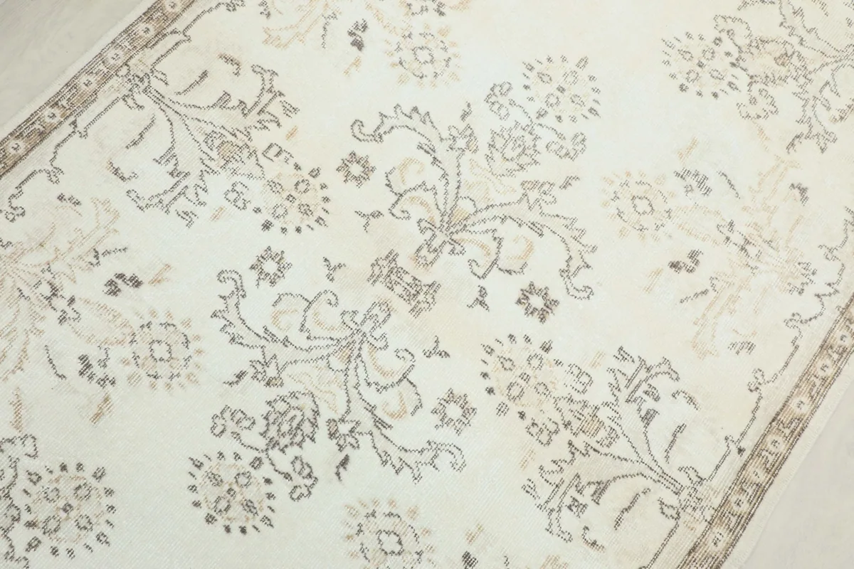 Detailed view of the central floral and medallion motifs in beige and gray on the ivory field