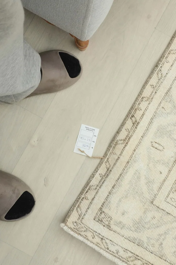 Close-up of a person's feet next to the rug, showing a size tag for scale and texture