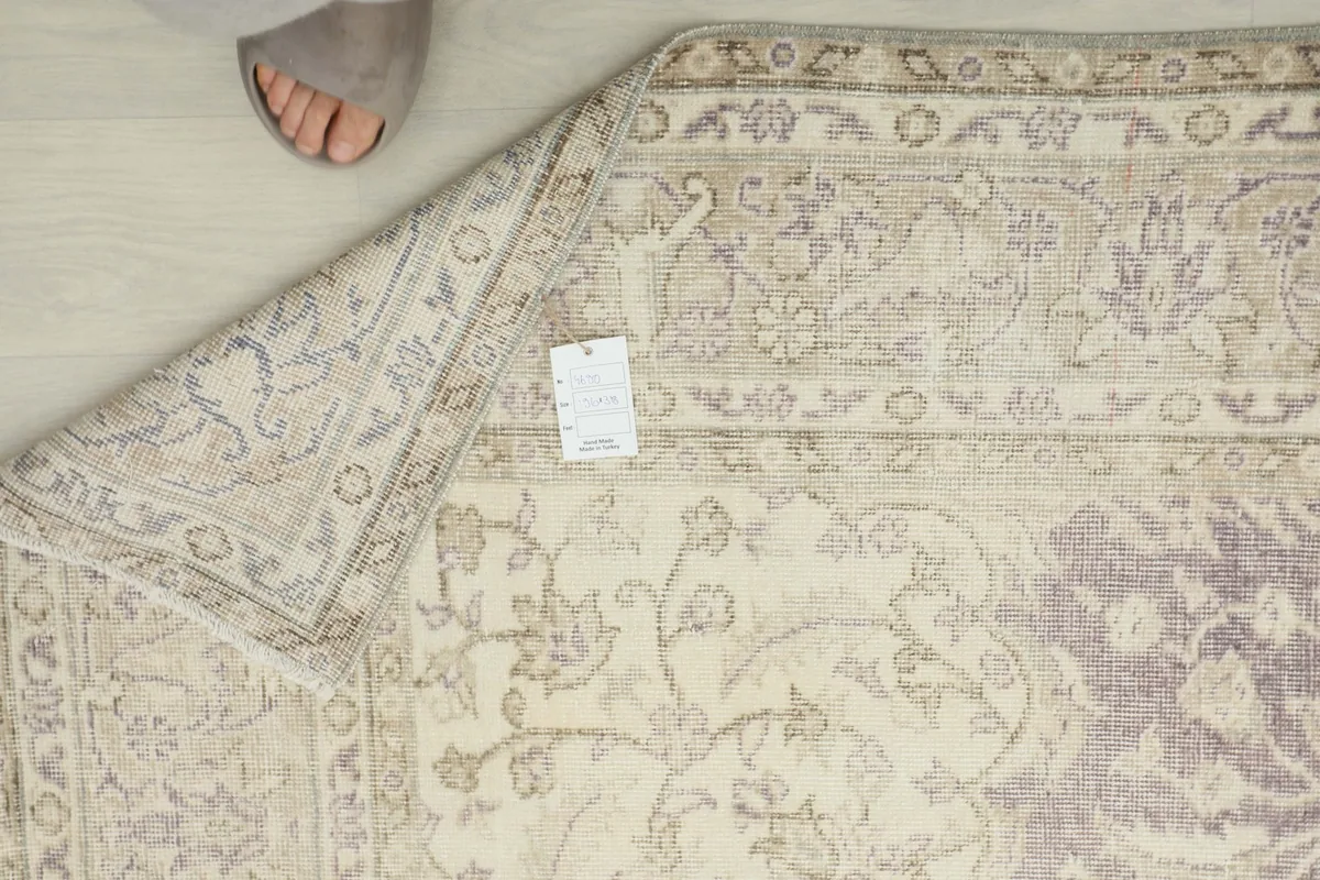 Overhead detail of the back of the rug with a corner folded, showing the hand-knotted construction and tag.