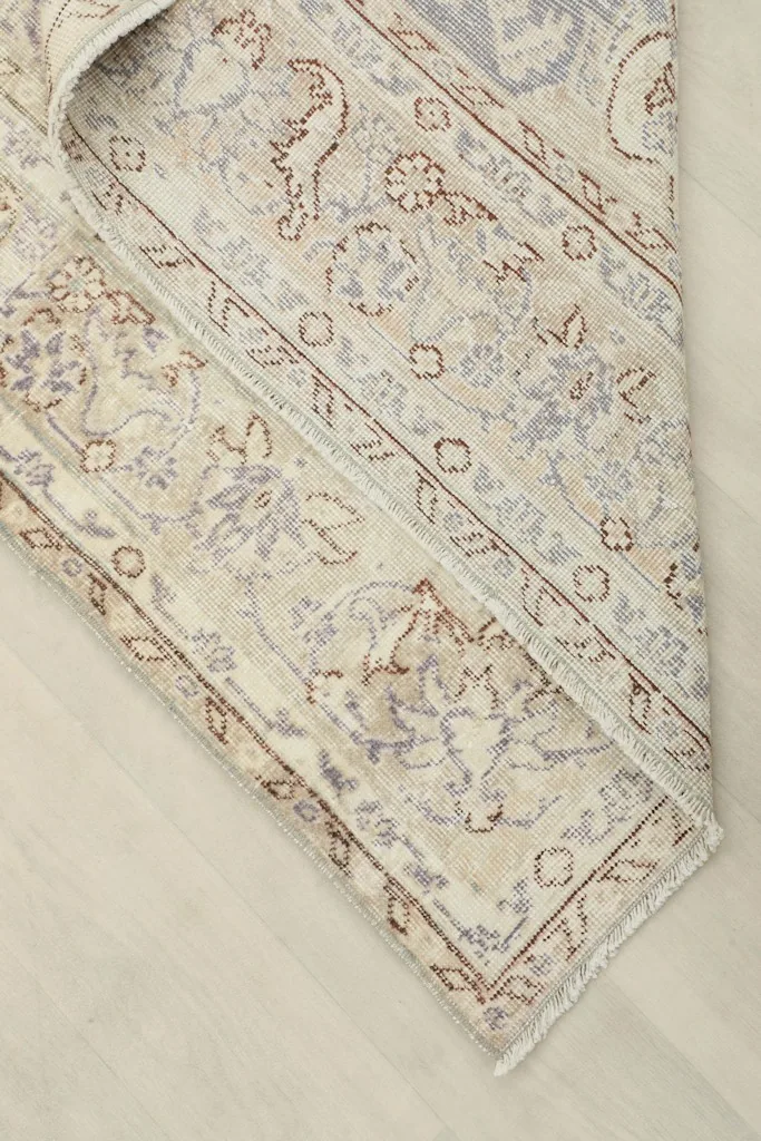 Corner of the vintage rug folded back, showing the cotton foundation and reverse side of the knotting.
