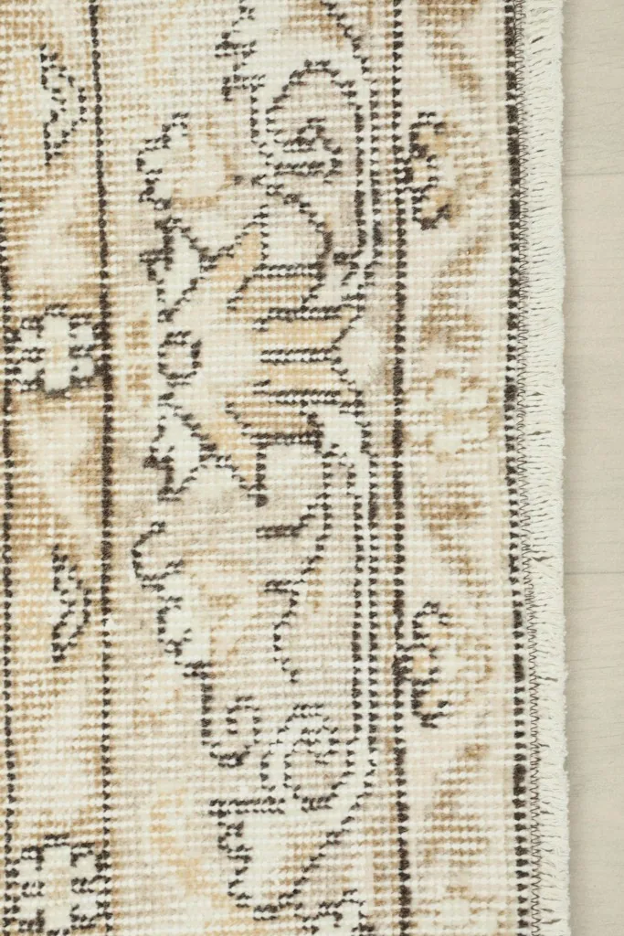 Detail of the rug's border design and short fringes, highlighting the muted tan and gray patterns.