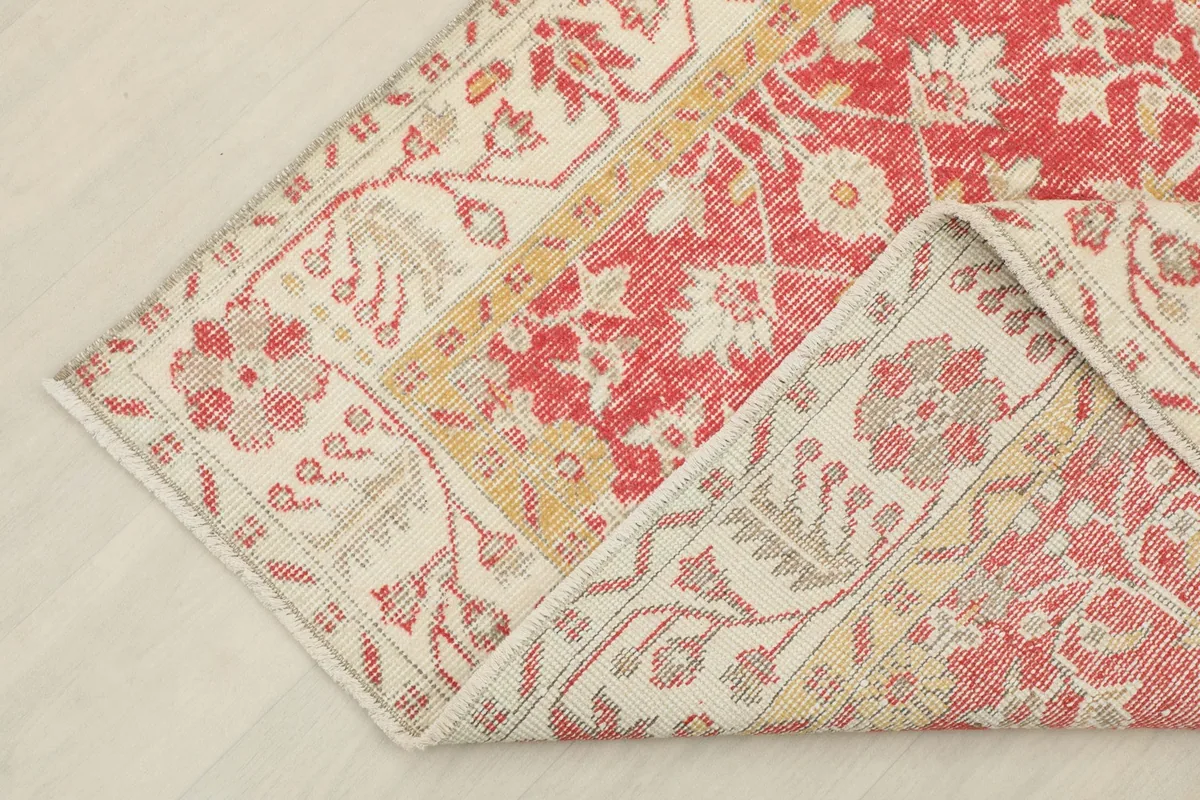 Corner of the red floral rug folded back, revealing the reverse side and knotting detail.