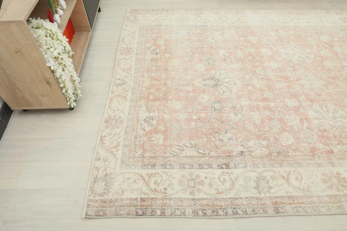 Close-up angle showing the cream border with floral motifs and the faded rose field of the vintage rug.