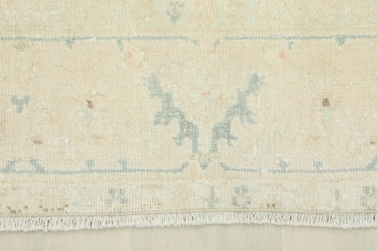 Detailed view of the rug's short fringe and the edge of the cream border with subtle blue elements.