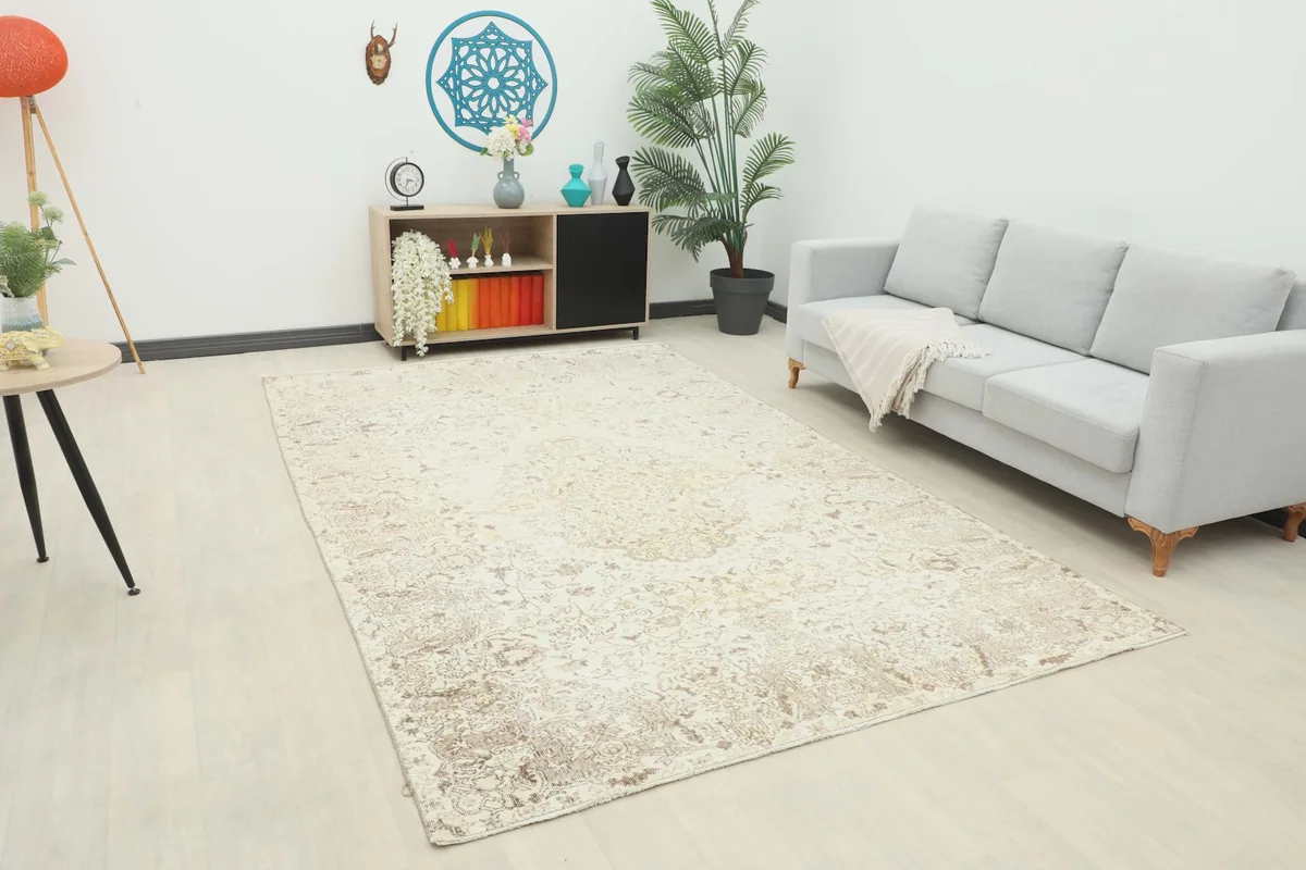 Ivory and beige vintage Anatolian rug displayed in a room setting with a sofa and side table.