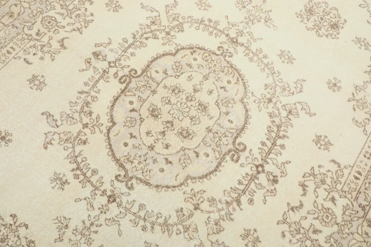 Detailed view of the central medallion pattern and surrounding floral elements in beige on ivory.