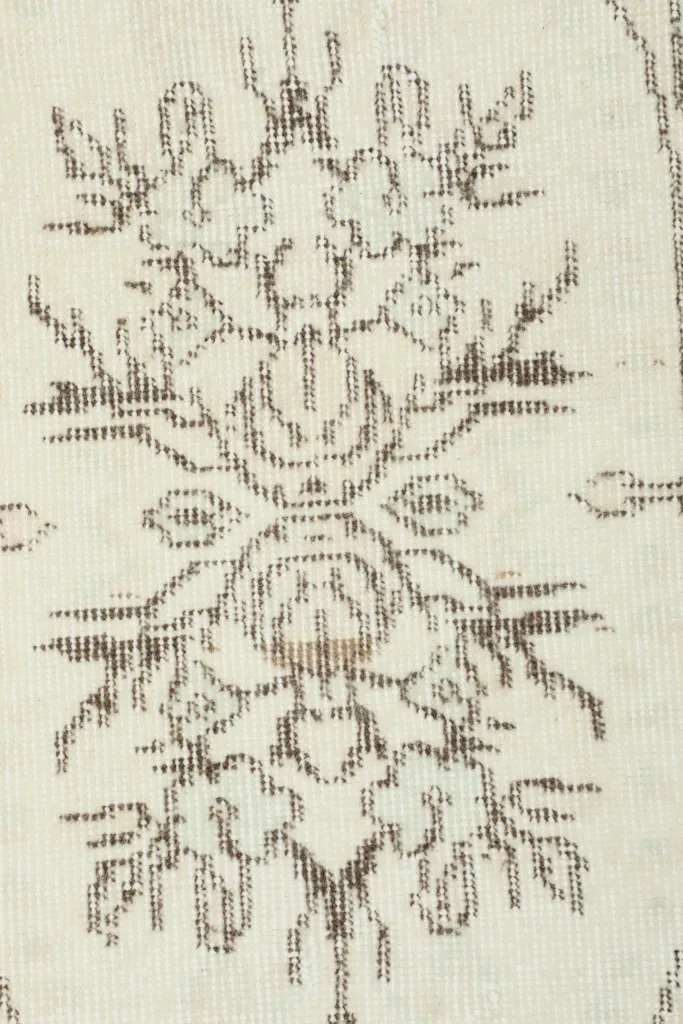 Close-up of a faded brown floral motif on the ivory field, showing hand-knotted texture.