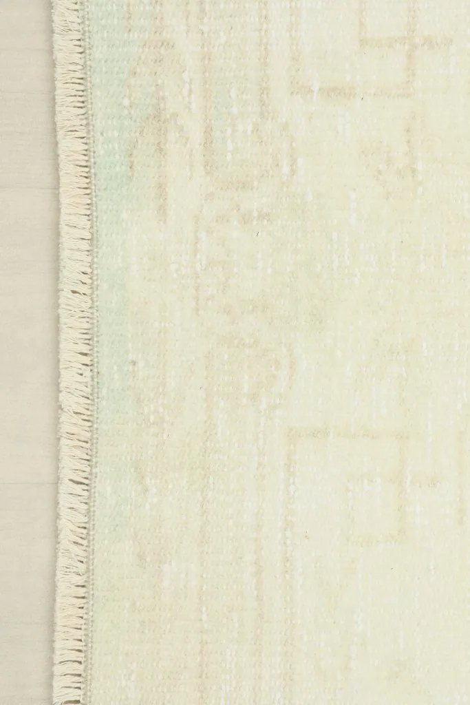 Side view showing the short, natural ivory fringes and the edge of the hand-knotted rug.