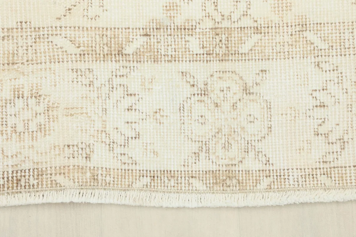 Close-up of the rug's border, revealing the subtle tan and cream patterns and short fringes.