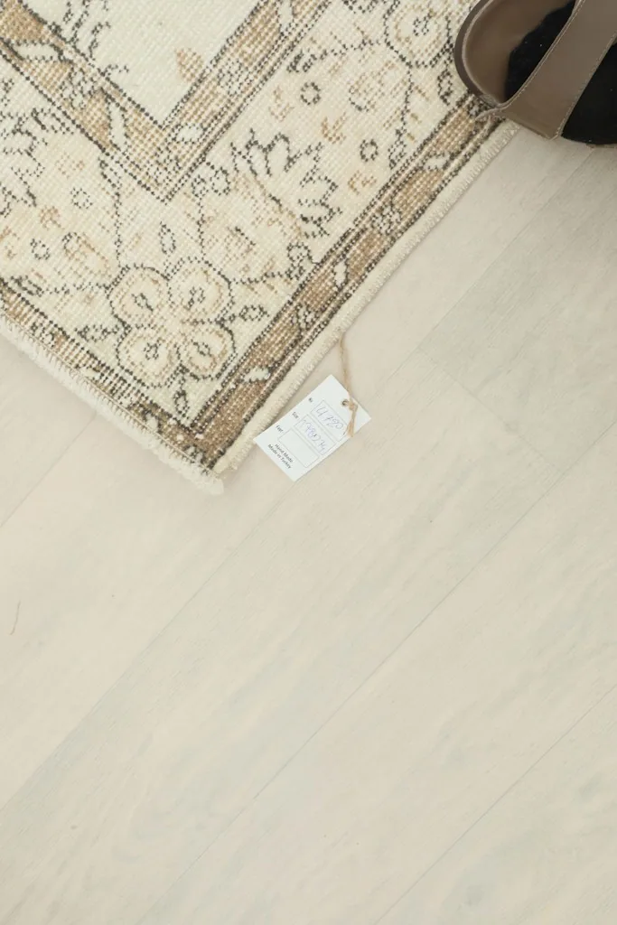 Corner of the rug with a product tag, showing the light wood floor beneath.