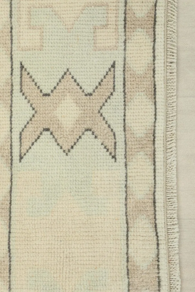 Detail of the rug's border, featuring alternating tan tribal elements and subtle fringe