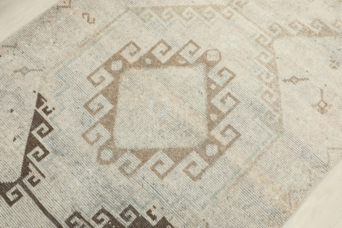 Detailed shot of a central geometric medallion in tan, with surrounding beige pile texture.
