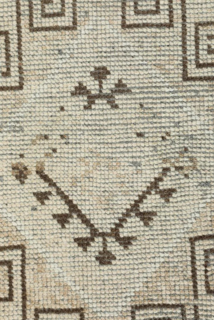 Macro view of a small, intricate tribal motif in brown, showcasing the hand-knotted wool pile.