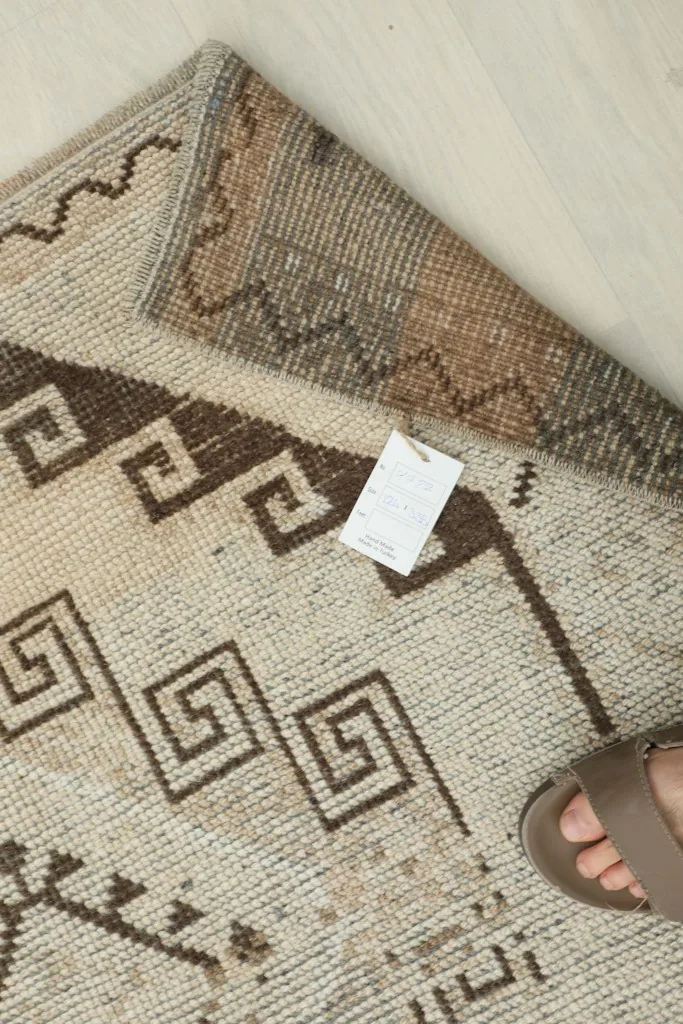 Overhead view of a corner of the rug with a tag, showing the intricate brown geometric designs.