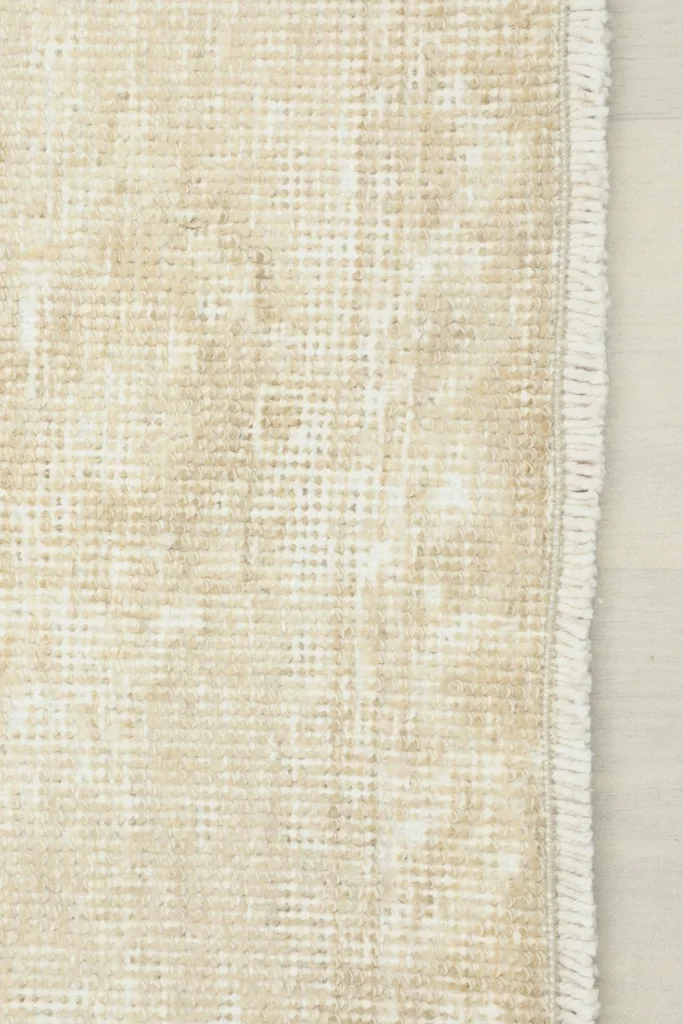 Detail of the short, clean fringe and the edge of the beige hand-knotted runner rug.
