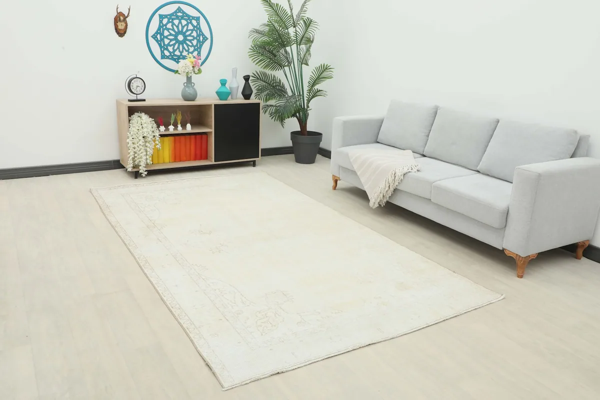 Ivory vintage Anatolian rug displayed in a modern living room setting with a sofa and cabinet.