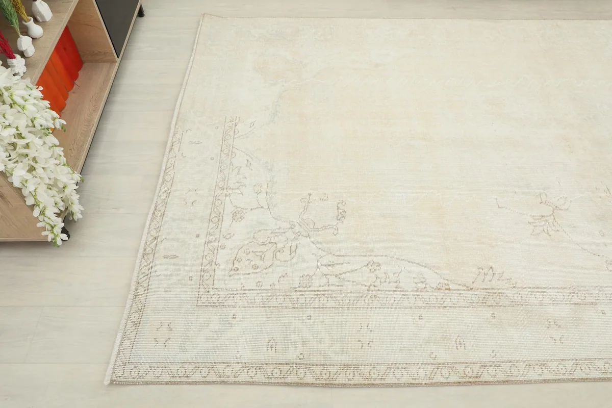 Corner detail of the rug, showing the faded beige motifs and the overall ivory tone.