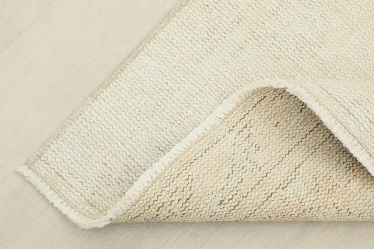 Corner of the rug folded back to show the cotton foundation and the reverse side of the hand-knotted weave.