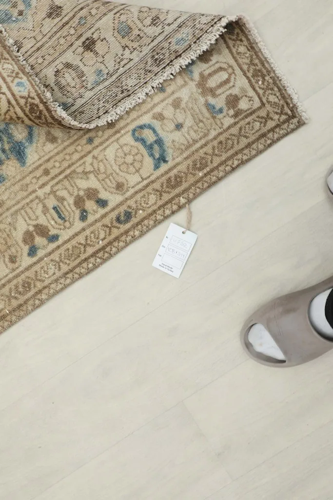 Top-down view of the rug's edge with a tag and a pair of slippers for scale