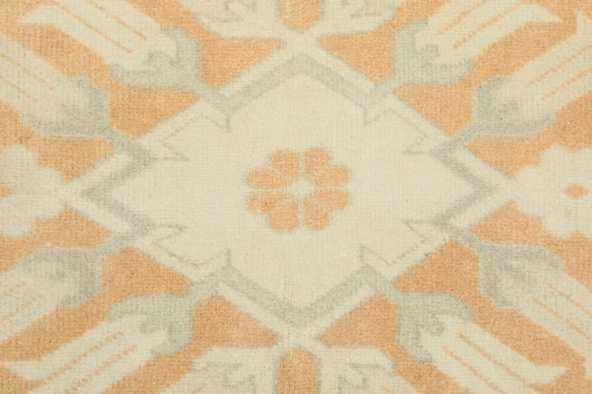 Close-up on a single floral geometric motif within the rug's orange central field.