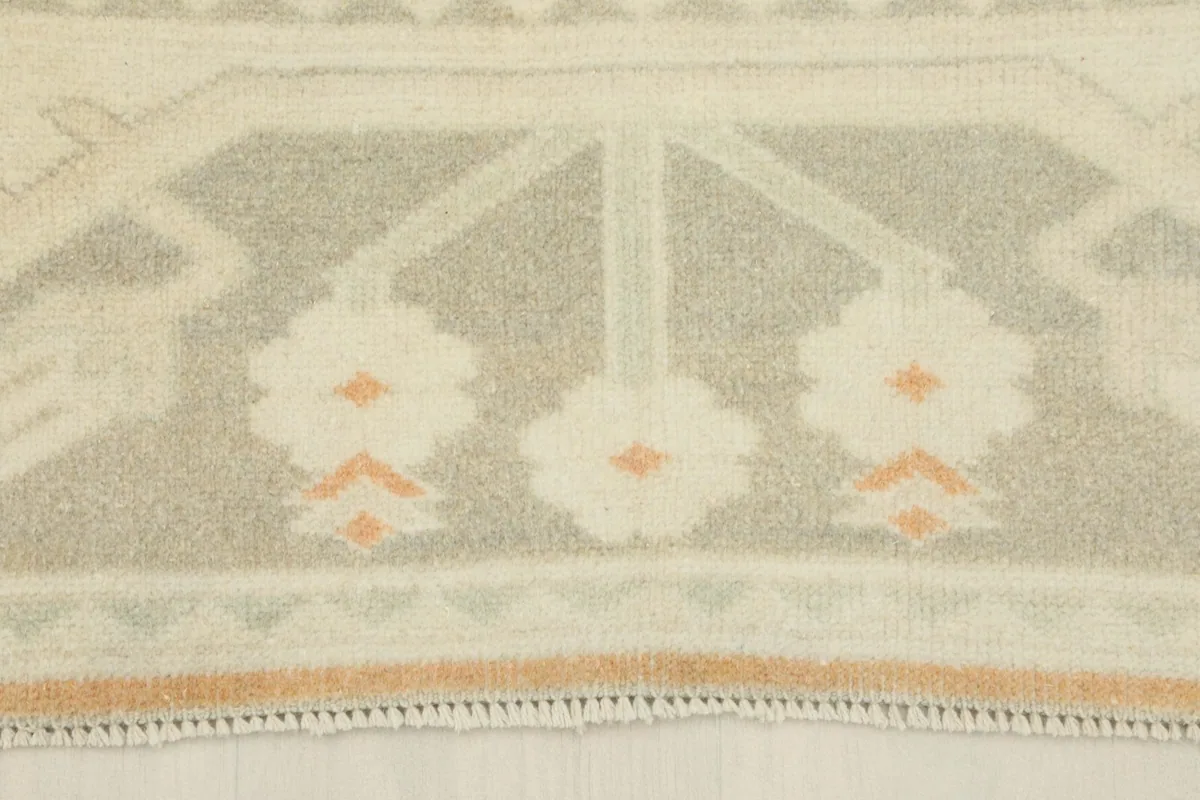 Detailed view of the rug's border, showcasing the gray and ivory patterns and fringe.