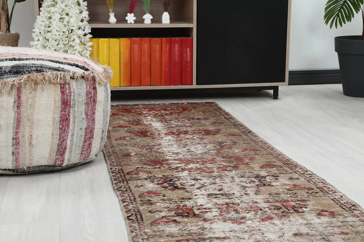 Close-up angle showing the distressed beige and red pattern of the runner rug next to a pouf.