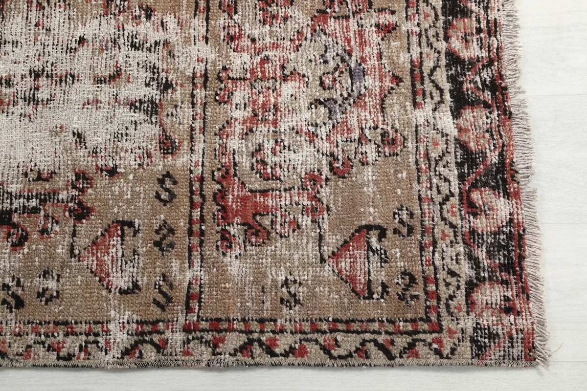 Detailed view of the rug's distressed wool pile, showcasing beige, red, and black geometric motifs.