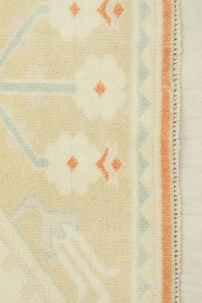 Edge detail of the rug, showing the hand-knotted wool pile and the rust-colored side finish.