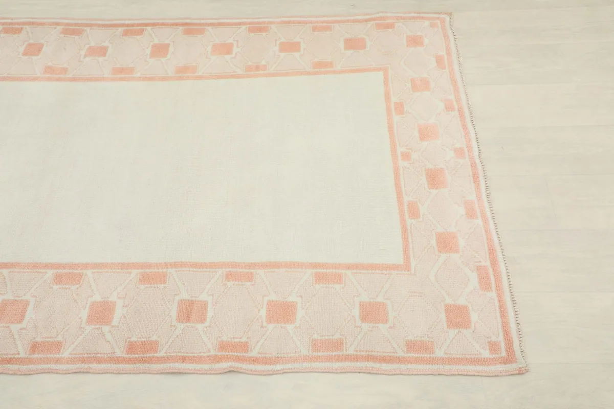 Close-up view of the rose geometric border and ivory field of the hand-knotted rug